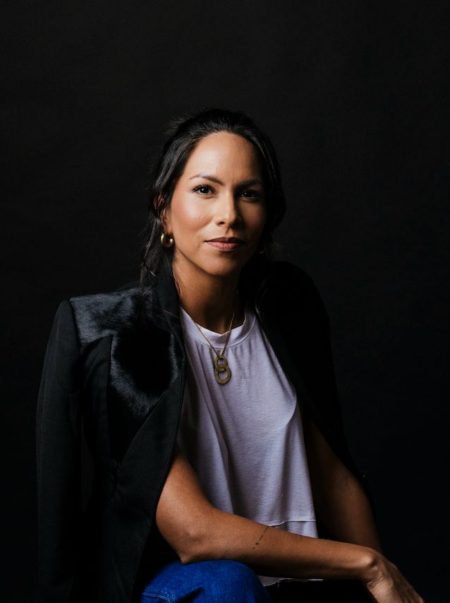 Marie Berry. Woman wearing a white top and blue pants with a dark background